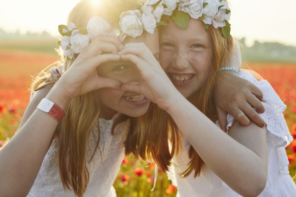To jenter med blomsterkranser i håret som lager et hjerte