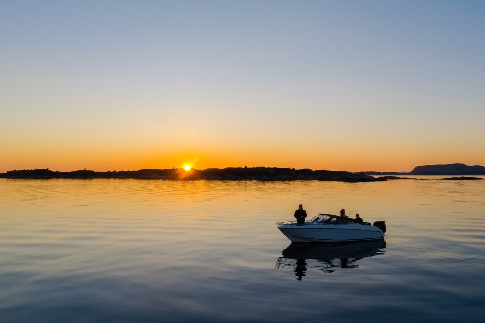 En båt på stille vann under en vakker solnedgang, med øyer i horisonten
